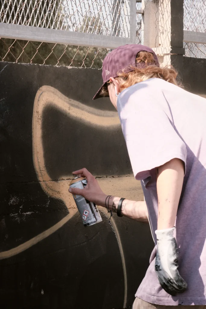 Close-up detail of a graffiti artist's hand using a yellow spray paint can to draw on a black wall.