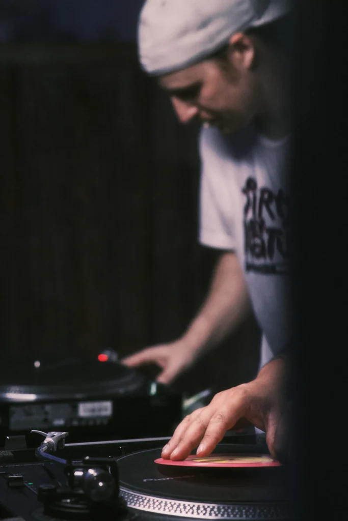 Close-up on a DJ's hand manipulating a red vinyl record on a turntable during a night sound system session.
