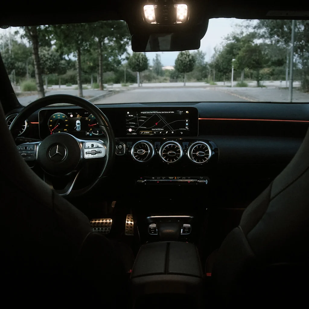 Interior view of Mercedes-Benz A-Class from driver's seat, showing digital dashboard, steering wheel, infotainment screen, and metal pedals