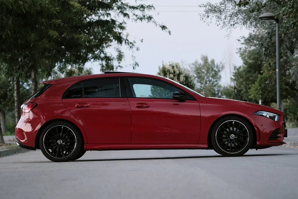 Clean side profile shot of a red Mercedes A-Class hatchback with black roof and multi-spoke black alloy wheels parked outdoors.
