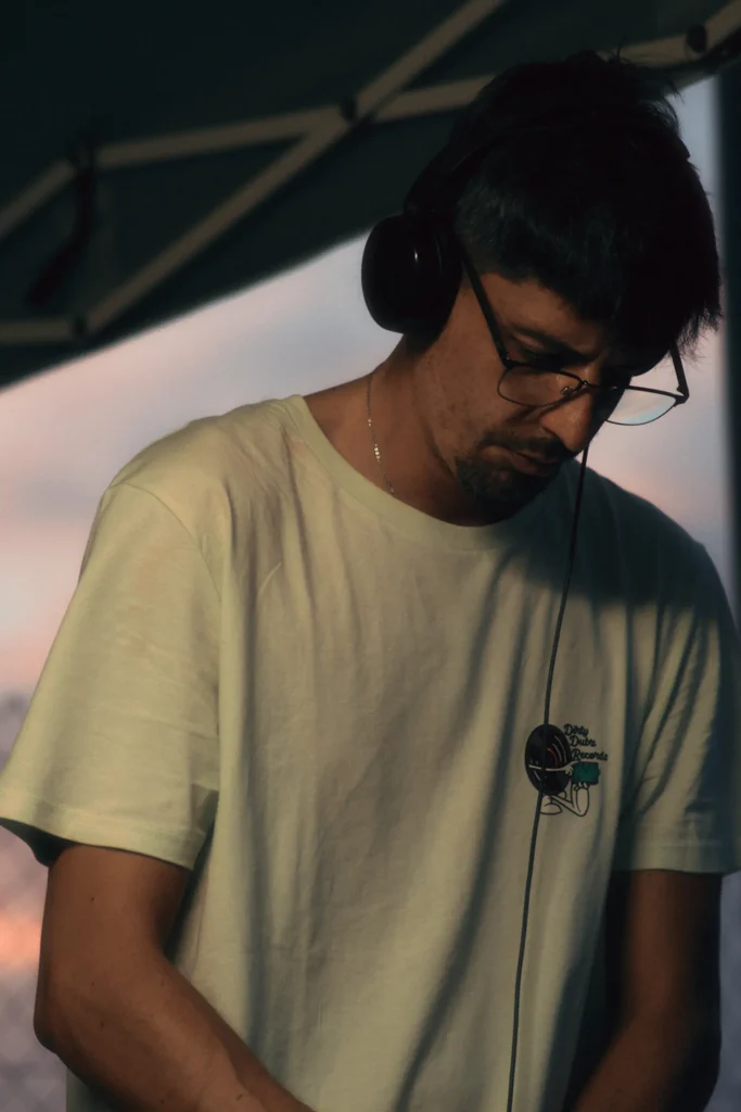 Portrait of a DJ with glasses and headphones focused on mixing music outdoors during the sunset/twilight hour.