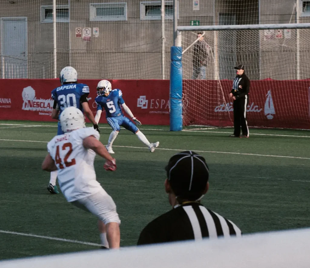 Action photo of an American football player preparing to receive a kick near the end zone, referee in background.