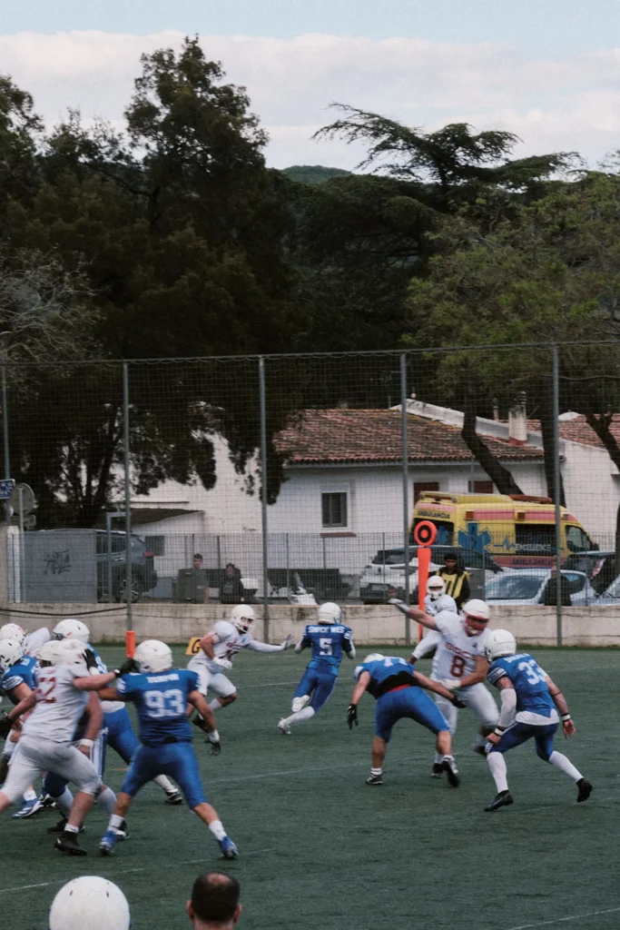 Wide action photo capturing a full-team play on the field, showing the intensity and the presence of medical staff (ambulance) in the background.
