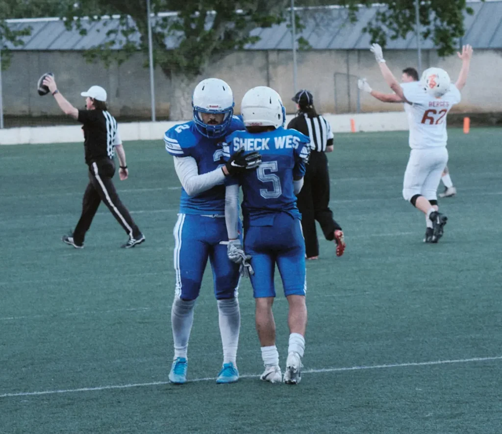 Action photo of two players hugging in celebration or support after a crucial play, capturing sports emotion with referee nearby.