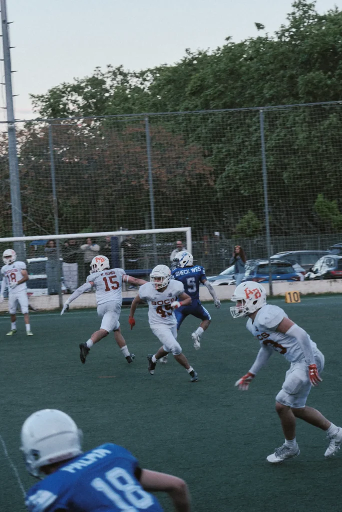 Dynamic shot of an American football run play, with players in motion during the evening game, showcasing field depth and action.