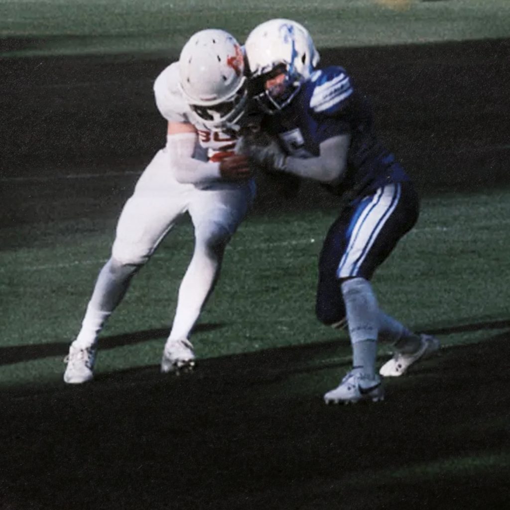 Close-up action shot of two football players engaged in a tackle under challenging dark and low-light field conditions.