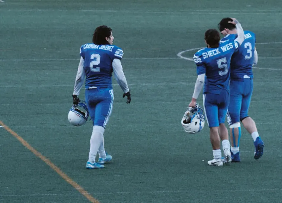 Post-game atmosphere photo showing American football players (including Sheck Wes) walking off the field, highlighting team camaraderie.