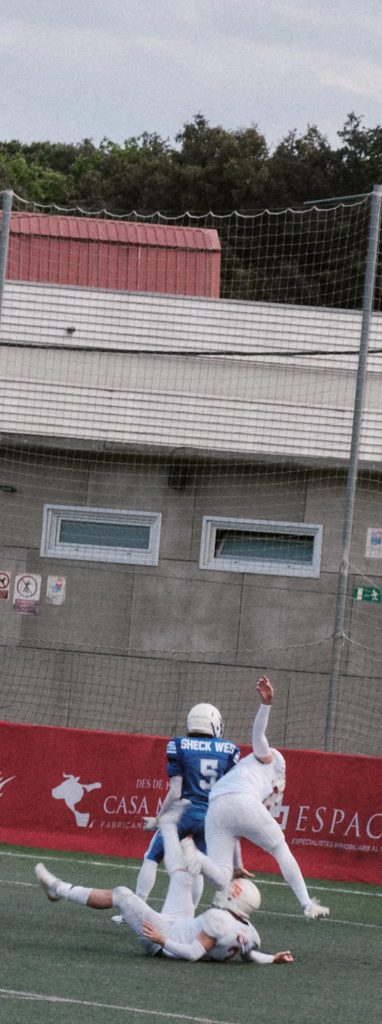 Vertical action photo of players in the end zone, showing a low tackle and struggle for a touchdown.