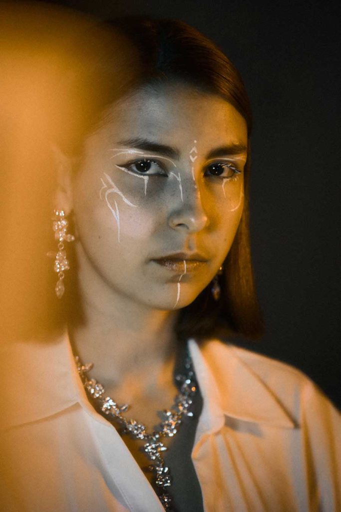 Avant-garde editorial beauty portrait, showcasing artistic makeup and high-end jewellery under warm cinematic lighting for fashion campaigns