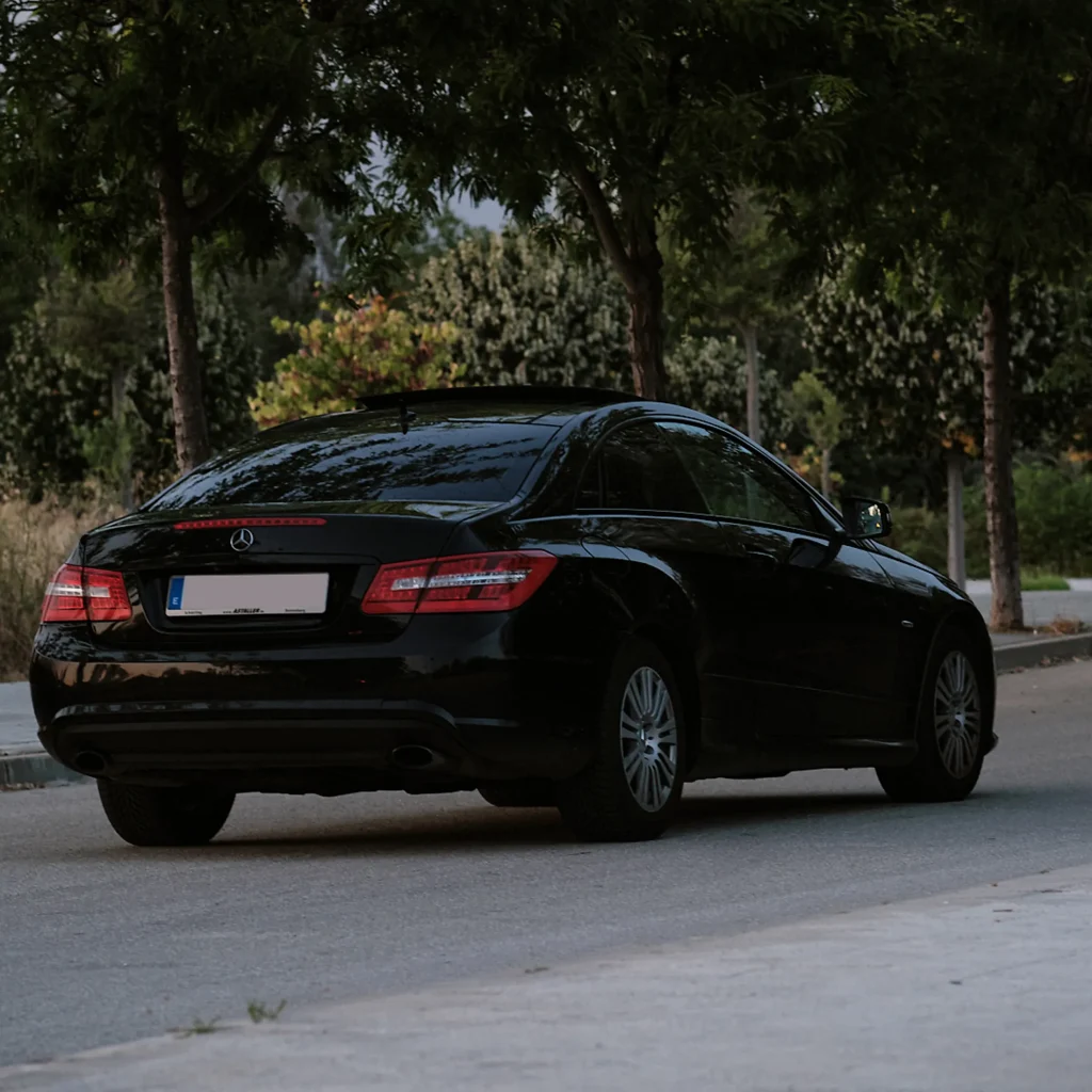 Detailed close-up of the modern headlight (LED or Xenon) and the textured front grille of the black car, emphasizing the clean finish.