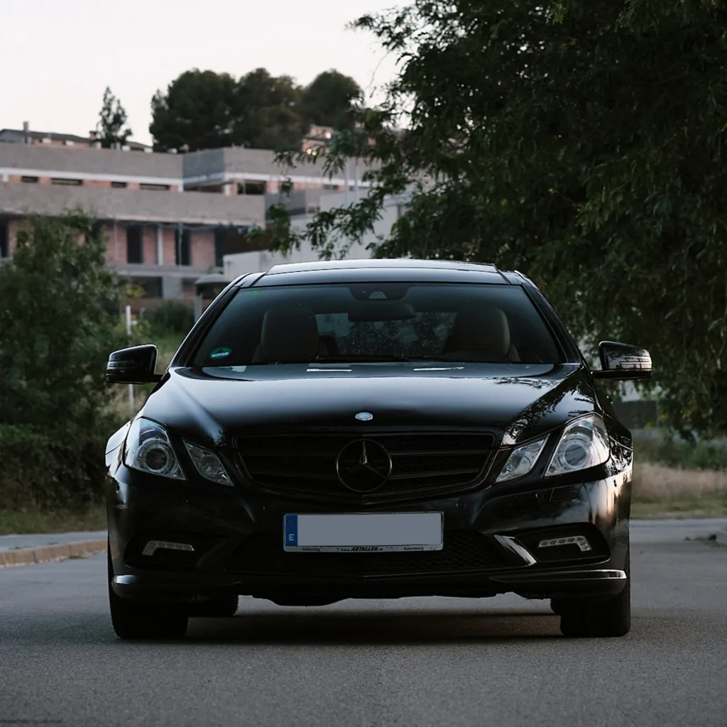 Low-angle close-up of the rear alloy wheel and tire of the black Mercedes E-Class C207, showing the glossy black bodywork.