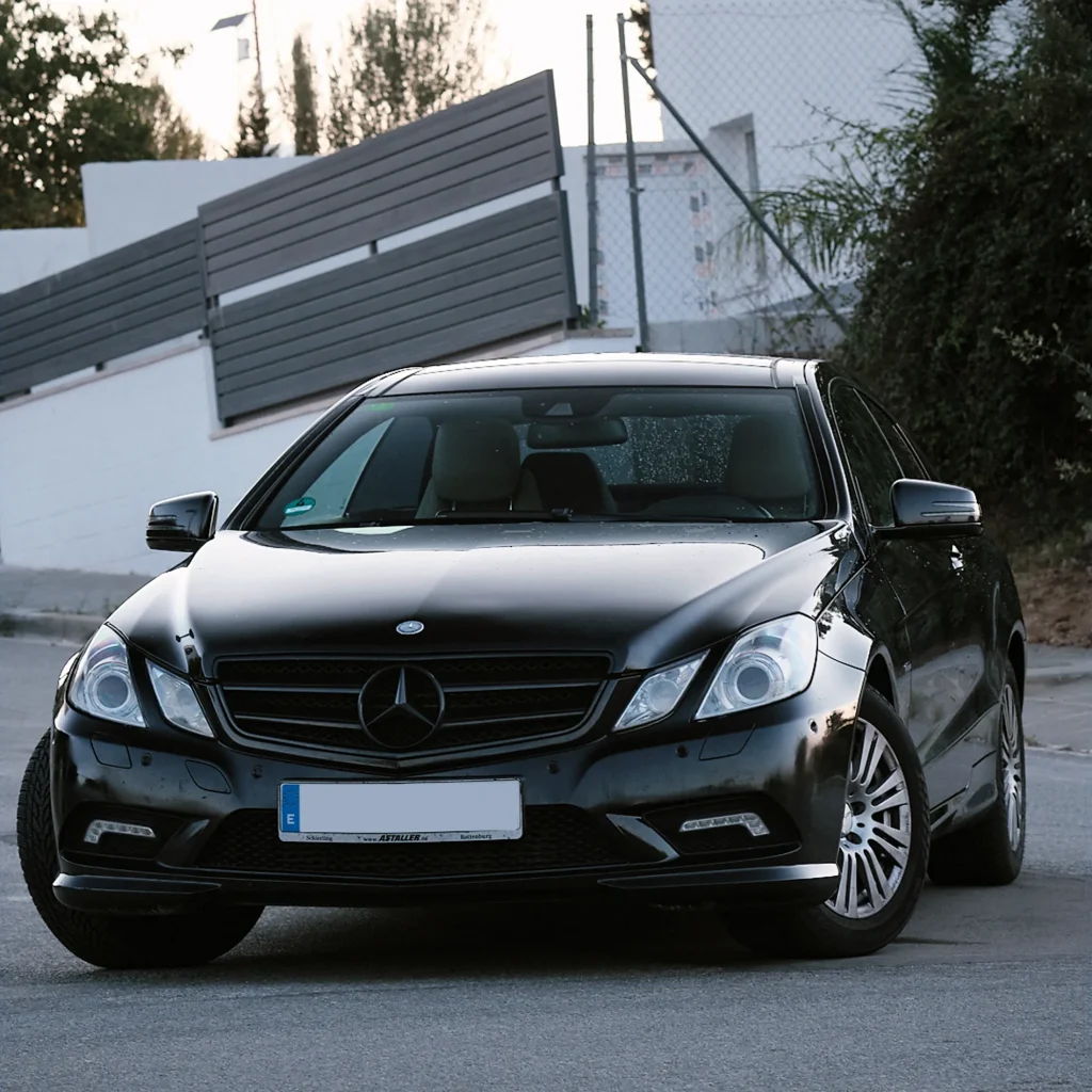 Dynamic side profile shot of a glossy black Mercedes-Benz E-Class Coupé (C207) parked on asphalt, emphasizing sleek lines.