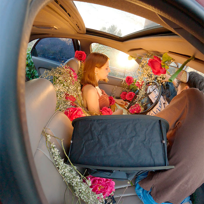 Behind the scenes of the surreal car scene: crew setting up lighting and filming the actress surrounded by roses inside the car