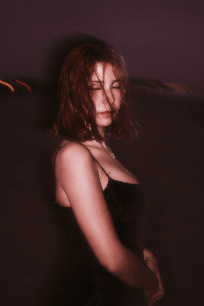 Portrait of the Burnout protagonist on a beach with eyes closed, hair blowing in the wind, evoking a sense of release or exhaustion