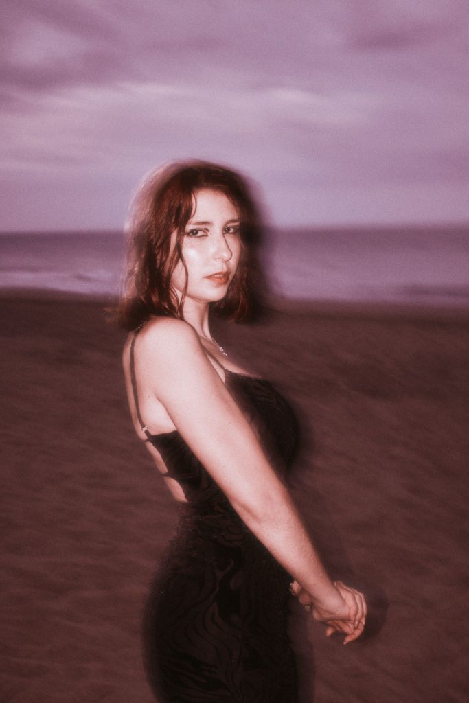 ntense portrait of the Burnout protagonist on a reddish beach with a blurry purple sky, looking directly at the camera