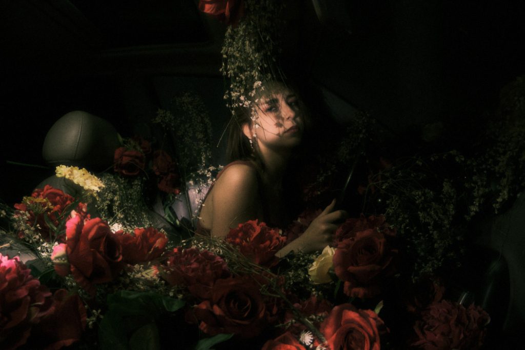 The main character of Burnout in contemplation, submerged in roses and baby's breath inside the car.