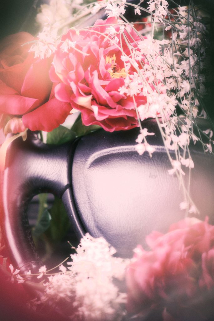 Soft-focus detail of the car's steering wheel obscured by red flowers, giving a dreamlike effect.
