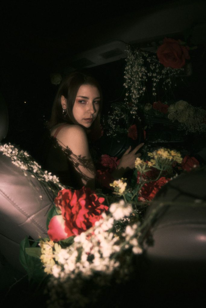 The protagonist of Burnout, partially covered by shadows, sitting among roses in the car at night.
