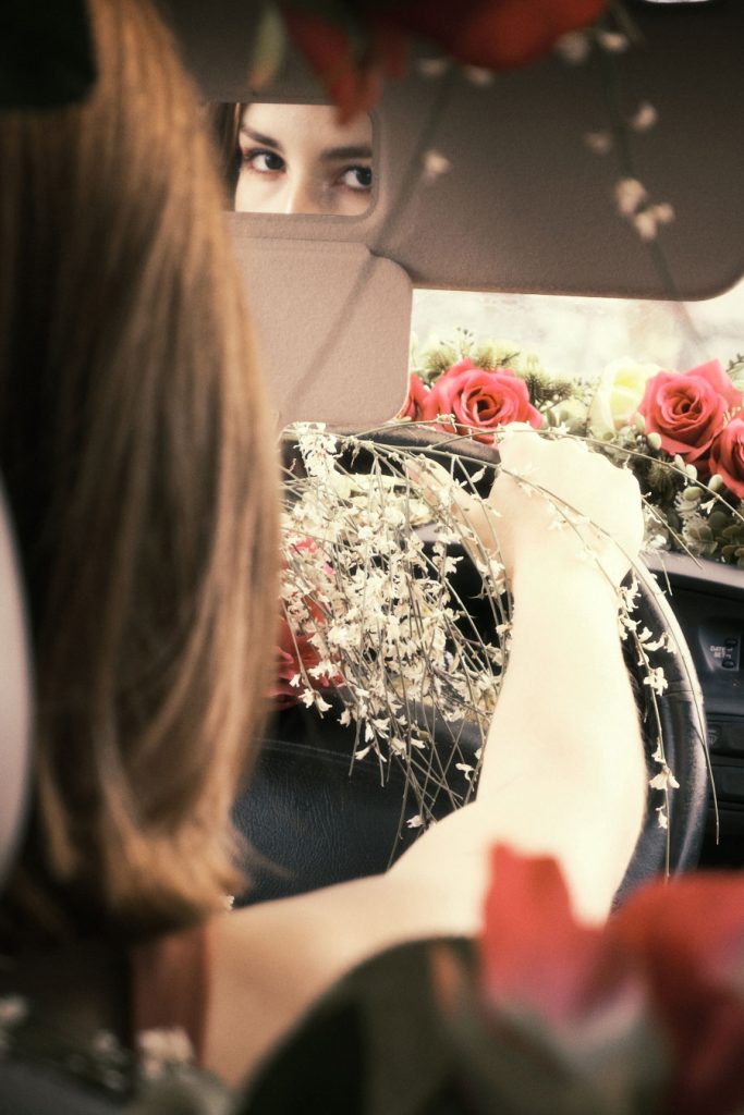 Close-up of the protagonist's eyes reflected in the car's vanity mirror, holding white flowers