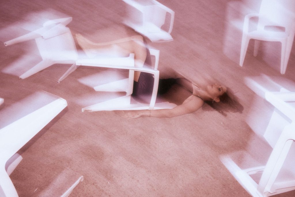 Top-down shot of the Burnout protagonist lying amidst scattered white chairs on a reddish beach, with motion blur effect