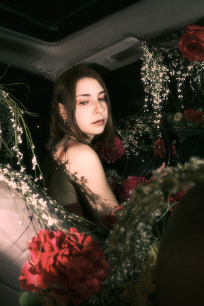 Stylized portrait of the woman in the rose-filled car scene, with pink makeup reflecting the lighting.