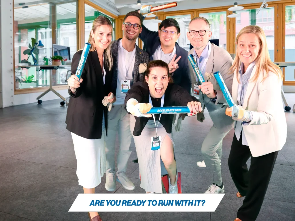 Group photo booth picture of five business people running and posing dynamically in a bright office setting for the Accelerate 2025 event.