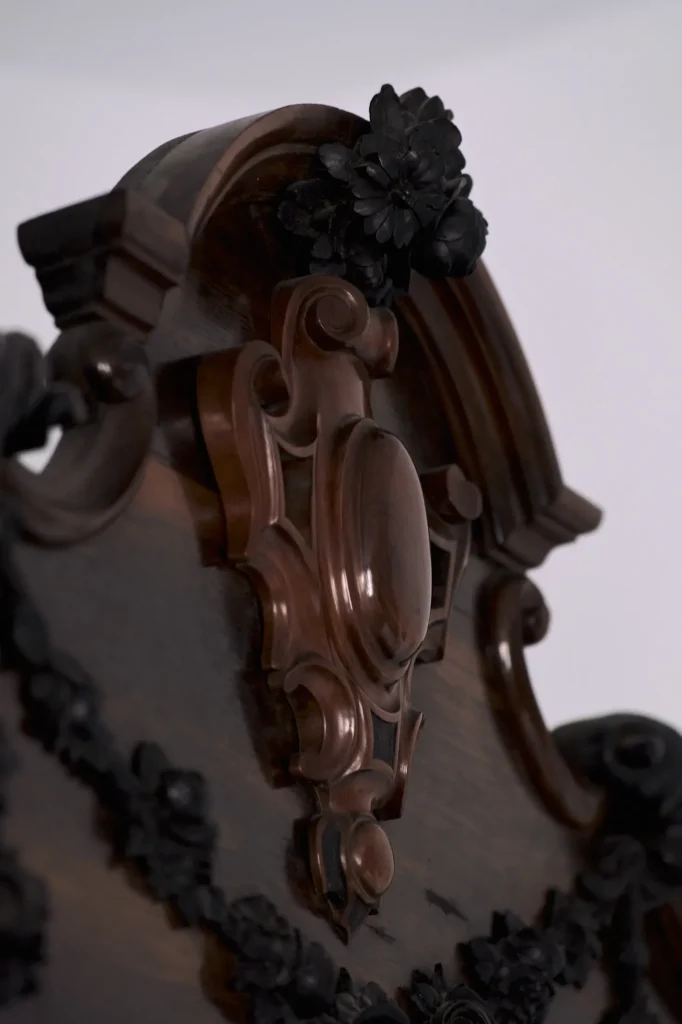Macro detail of a piece of dark carved wooden furniture, possibly a headboard or armoire, showcasing intricate floral and baroque relief designs.