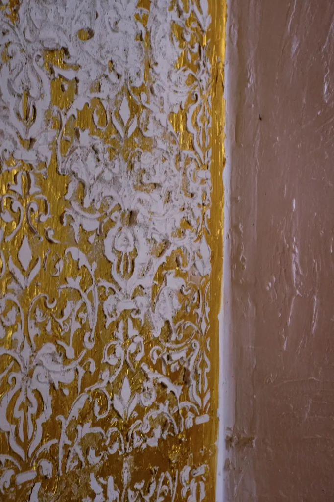Close-up detail of an ornate wall texture in Castell Granadella, featuring white stucco over a distressed gold or yellowish surface.