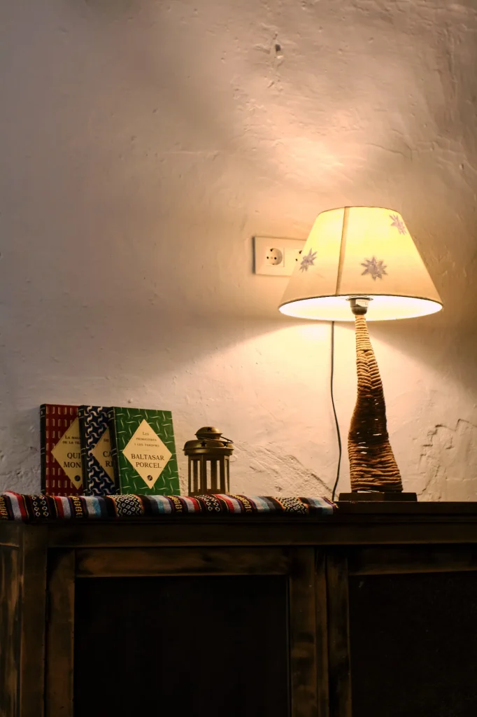 Nightstand or cabinet close-up with a glowing decorative lamp and a stack of books, highlighting the warm lighting and textured wall of the accommodation.
