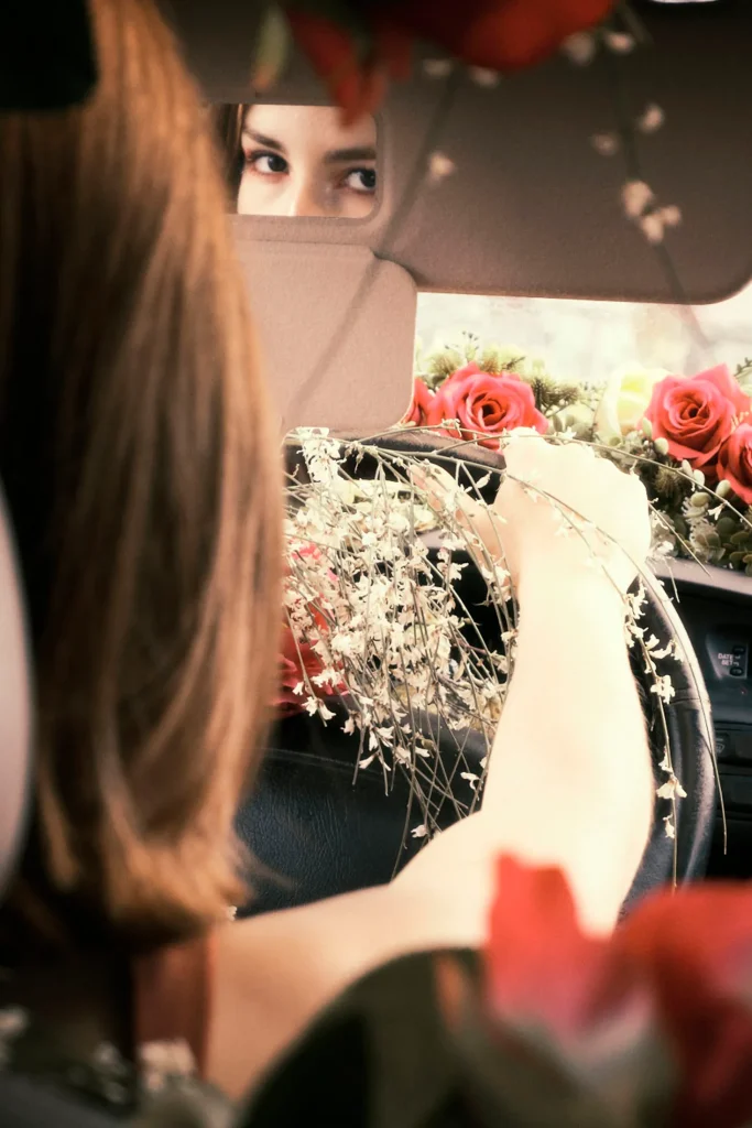 Conceptual close-up of a woman's reflection in a car's vanity mirror, holding a bouquet, capturing an intense gaze and intimate framing.