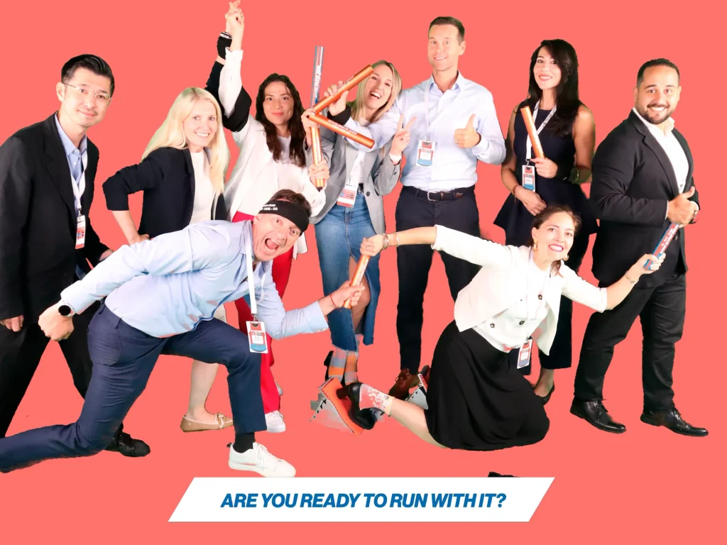 Group photo of eight professionals posing creatively on a red background with fun props, promoting the 'Are you ready to run with it?' theme.