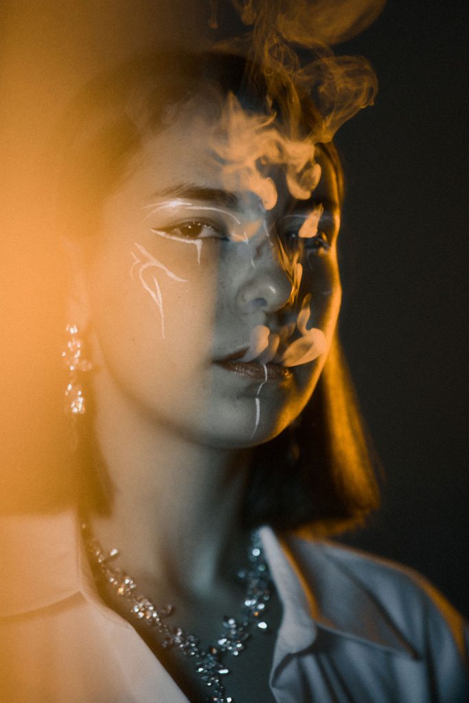 Close-up editorial portrait with artistic face paint and smoke, capturing intricate details of high-end jewellery and avant-garde beauty aesthetics