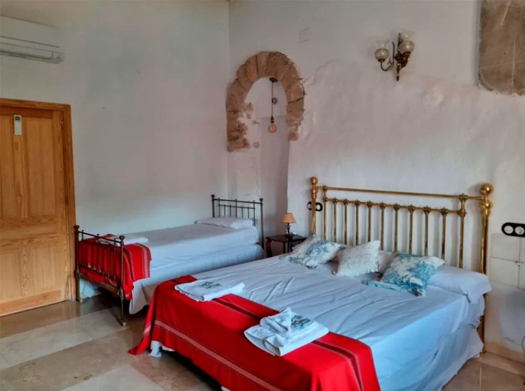 Previous photo (low quality) of a suite bedroom with a large brass bed frame, a secondary bed, and a wooden door.