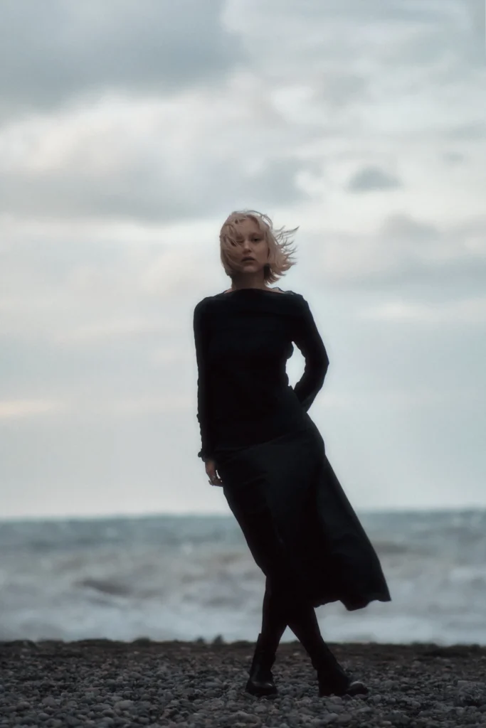 Wide lifestyle portrait of a woman standing near the sea in Mallorca, capturing a sense of contemplation and the vastness of the seascape.