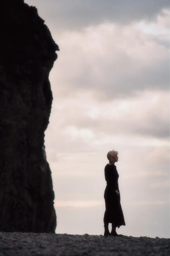 Close-up environmental portrait on the Mallorcan coast, focusing on the texture of the rocks and the subject's contemplative gaze.