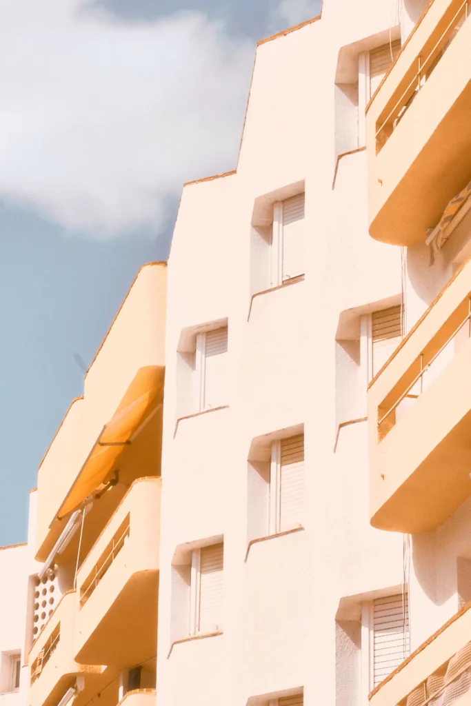 Minimalist and warm-toned lifestyle photography of a modern Mediterranean building facade with balconies and soft pastel colors, suitable for architecture and travel content in Spain or Portugal
