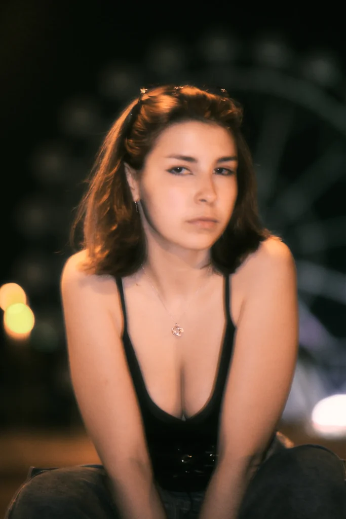 Fashion-focused night urban portrait of a woman in streetwear and small sunglasses, captured with intentional motion blur and neon glow effects.