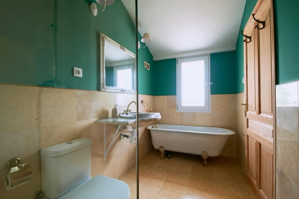 Vintage-style bathroom featuring a clawfoot bathtub, toilet, sink, and bold emerald green painted walls contrasting with light beige tiles.